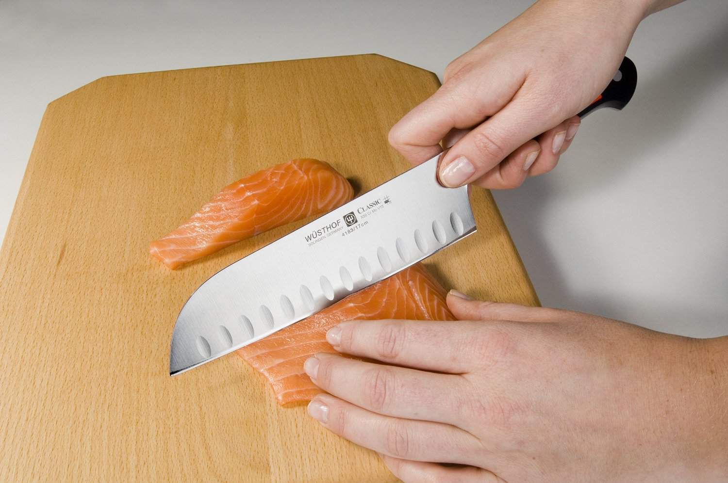Photo of a person slicing through fish meat using a Santoku knife